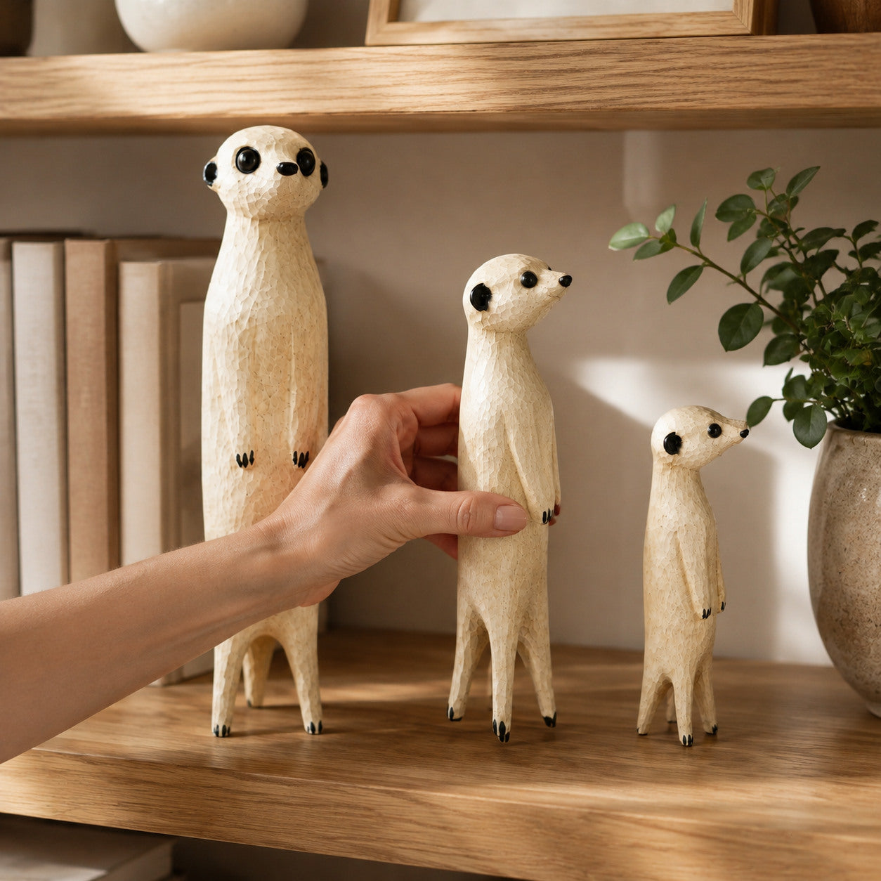 A hand arranging three wooden meerkat sculptures on a bookshelf
