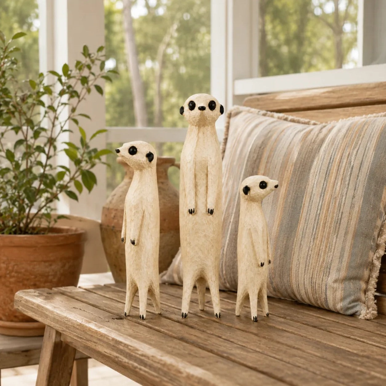 Customer's set of three wooden meerkat sculptures on an indoor bench